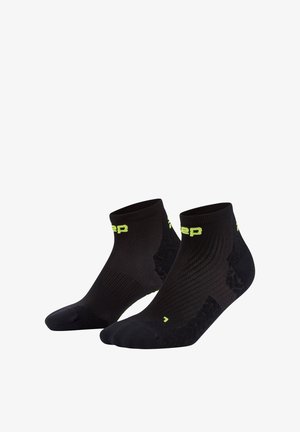 Schwarze Sportsocken mit einem kurzen Knöchelschnitt, ausgestattet mit einem strukturierten Muster und einem leuchtend gelben Logo. Hergestellt aus atmungsaktivem Material.