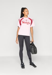 Rózsaszín sportpóló piros részletekkel és "Adidas" logóval, fekete leggingssel és fekete sporttáskával párosítva. Fekete cipő és zokni is látható.