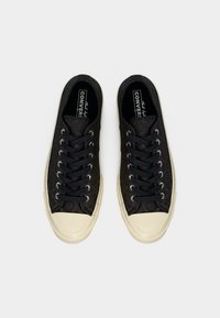 Ζευγάρι μαύρα Converse παπούτσια με υφή, με λευκές λαστιχένιες μύτες και σόλες, μαύρα κορδόνια, από πάνω σε λευκό φόντο.