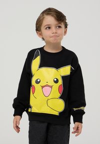 Czarna bluza z dużym, uśmiechniętym grafiką Pikachu w kolorze żółtym, z czerwonymi policzkami i czarnymi akcentami. Rybkowane mankiety i dekolt.