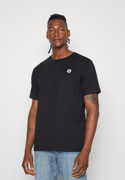 Svart crew-neck t-skjorte med korte ermer, laget av bomull, har en liten hvit logo på brystet, kombinert med lyseblå jeans.