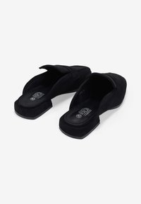 Zapatos de ante negros tipo mule con suela plana, que cuentan con un talón abierto y una parte delantera ligeramente elevada para mayor comodidad y soporte.