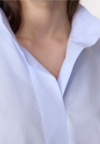 Jasnoniebieska bluzka z ostrym kołnierzykiem i czystym, minimalistycznym fasonem. Gładka tekstura, z subtelnym połyskiem i wyraźnymi liniami przy dekolcie.