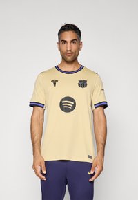Bež polo majica s crnim detaljima, okruglim ovratnikom i plavim rubom. Sadrži crni klub logo i kružni Spotify logo na prsima.