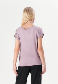 Light lavender short-sleeve t-shirt with a relaxed fit, soft texture, and a wide neckline, paired with black trousers.