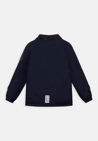 Navy blue jacket with long sleeves, elastic cuffs, buttoned collar, patch on left arm, and six-dot rectangular label at bottom back.