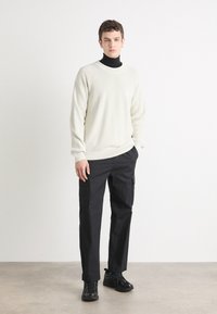 Maglione a coste beige chiaro, pantaloni cargo neri con tasche e sneakers nere. Design semplice e funzionale con una vestibilità rilassata.