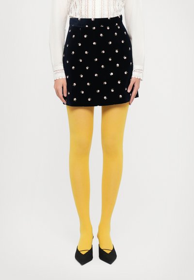 Must mustr ehk musta velvetist mini seelik, millel on lilleline tikand, koos kollaste sukkade ja mustade terava nina kontsadega. Valge pluus pitsdetailidega.