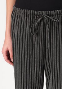 Pantalons de jogging à rayures noires et blanches avec une taille élastique et un détail à nouer. Présente une texture de tissu douce et un motif de rayures verticales.