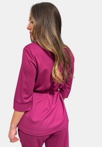 Blusa fucsia con vita annodata, maniche a tre quarti e una trama morbida. Il design è svasato con un orlo curvo.