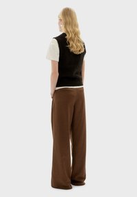 Zwarte gebreide sjaal over een wit T-shirt, gecombineerd met bruine wijde broek. Soepele textuur, losse pasvorm en eenvoudig ontwerp.