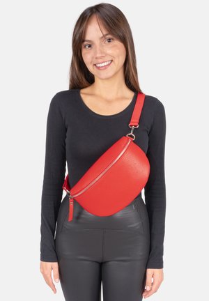 Red leather crossbody bag with a curved shape, textured finish, and a zipper closure, worn over a black long-sleeve top.