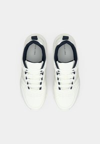 Balti sporta sporta apavi ar gludu ādas augšdaļu, teksturētiem akcentiem, tumši ziliem elementiem un plakaniem šņorēm. Sānos ir nelieli perforējumi.