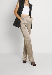 Beiga satintrosor med rak bendesign, med sidfickor och en jämn textur, i kombination med en svart västjacka med ränder.