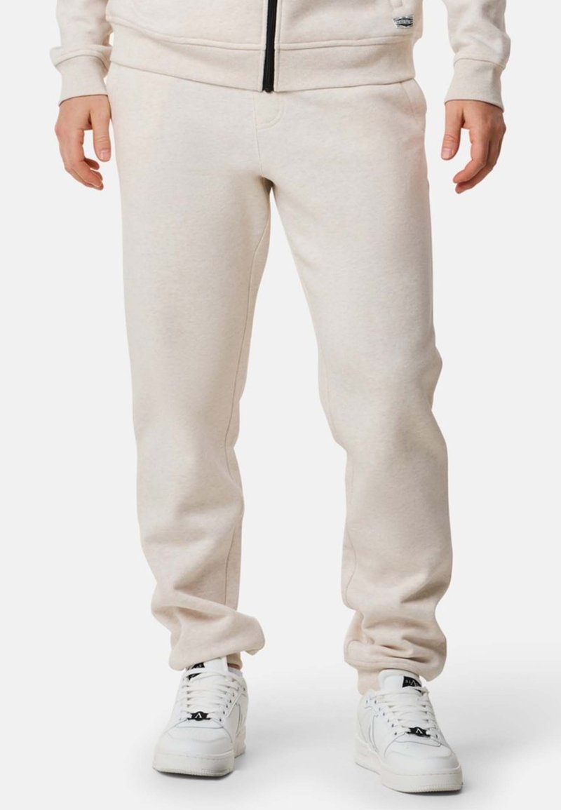 Beige mjukisbyxor med avslappnad passform, tillverkade av en mjuk bomullsblandning, med elastiska muddar och sidofickor. Kombinerade med vita sneakers.