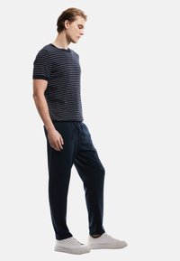 Navy-gestreiftes T-Shirt, kombiniert mit navy Jogginghosen. Das T-Shirt hat dezente weiße Streifen; die Hose besitzt eine lockere Passform und einen Kordelzugbund.