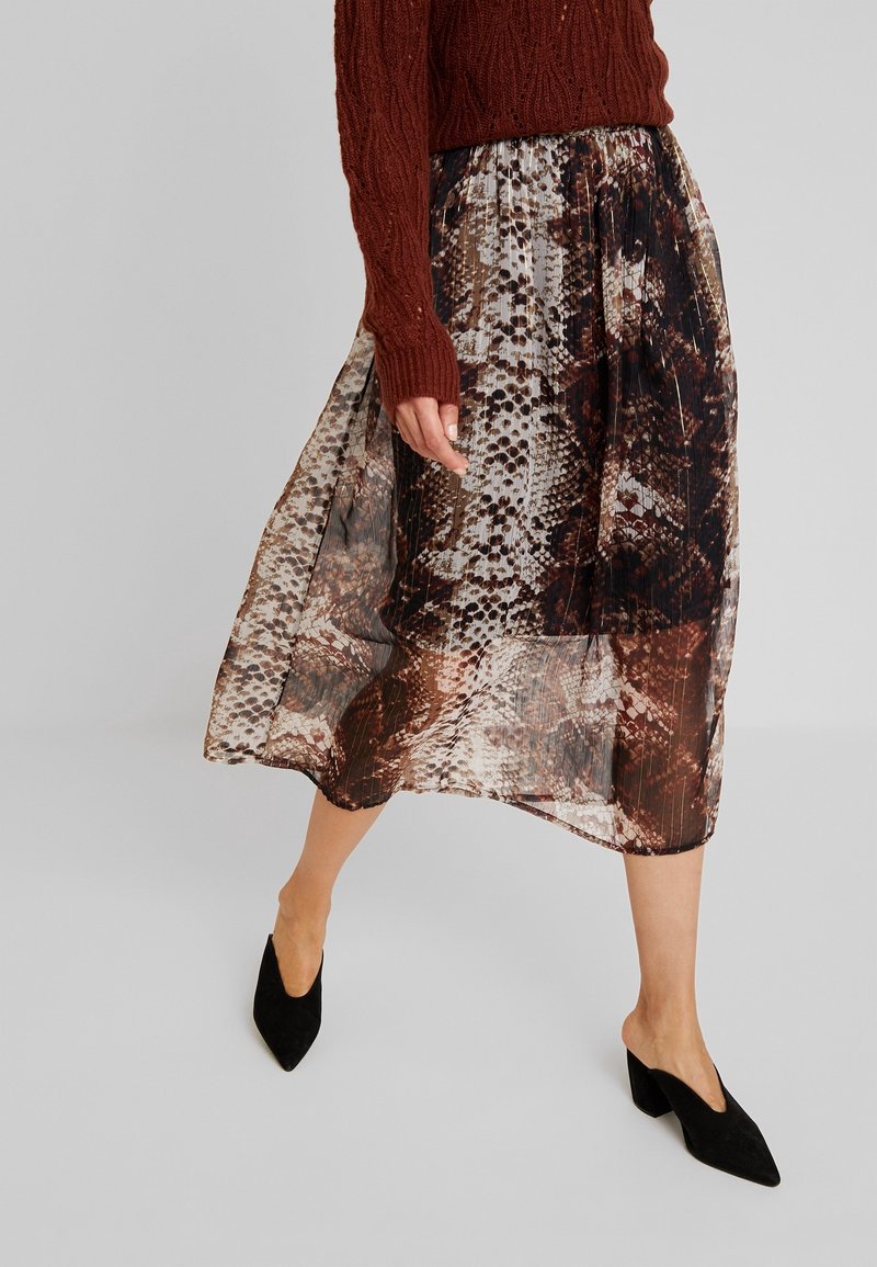 Flowy, sheer skirt with snake print in shades of brown and cream; mid-length with elastic waistband, paired with black pointed shoes.