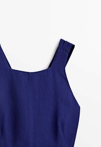 Ärmlös marinblå klänning med bred fyrkantig halsringning och plisserade axelremmar, liggande platt på vit bakgrund.