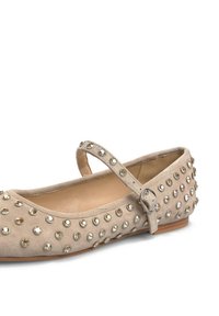 Bailarina de ante beige con tiras al estilo Mary Jane, adornada con tachuelas metálicas en la parte superior, suela plana y punta redondeada.