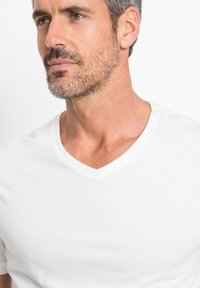 T-shirt bianca a V con scollo, realizzata in cotone morbido, caratterizzata da maniche corte, un design aderente e dettagli di cucitura minimalisti sul colletto.