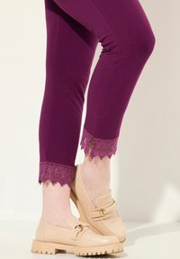 Leggings violets ajustés avec une bordure en dentelle aux chevilles, associés à des mocassins beiges avec une boucle décorative et une semelle texturée.