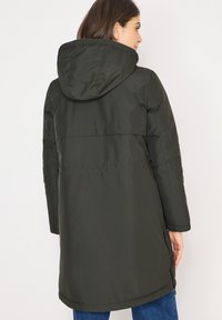 Ciemnozielona, parka z kapturem i wodoodporną powłoką, z taliowanym krojem, bocznymi zamkami i długością do połowy uda. Gładka faktura.