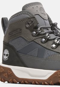 Botte de randonnée mi-haute imperméable grise avec des matériaux texturés, bout renforcé, œillets en métal et détail de logo sur le côté. Semelle en caoutchouc avec motif de grip.