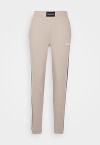 Beżowe spodnie dresowe wykonane z bawełny o zwężanym kroju, z czarnymi paskami po bokach oraz metką na talii z logo "Calvin Klein".