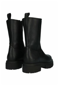 Botas de cuero negro hasta el tobillo con textura lisa, cremallera lateral y suelas de goma gruesa con un patrón de dibujo. Tiradores para facilitar su puesta.