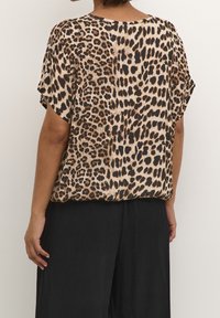 Haut à manches courtes en imprimé léopard, présentant une coupe décontractée, une texture soyeuse et un col arrondi, associé à un pantalon noir ample.