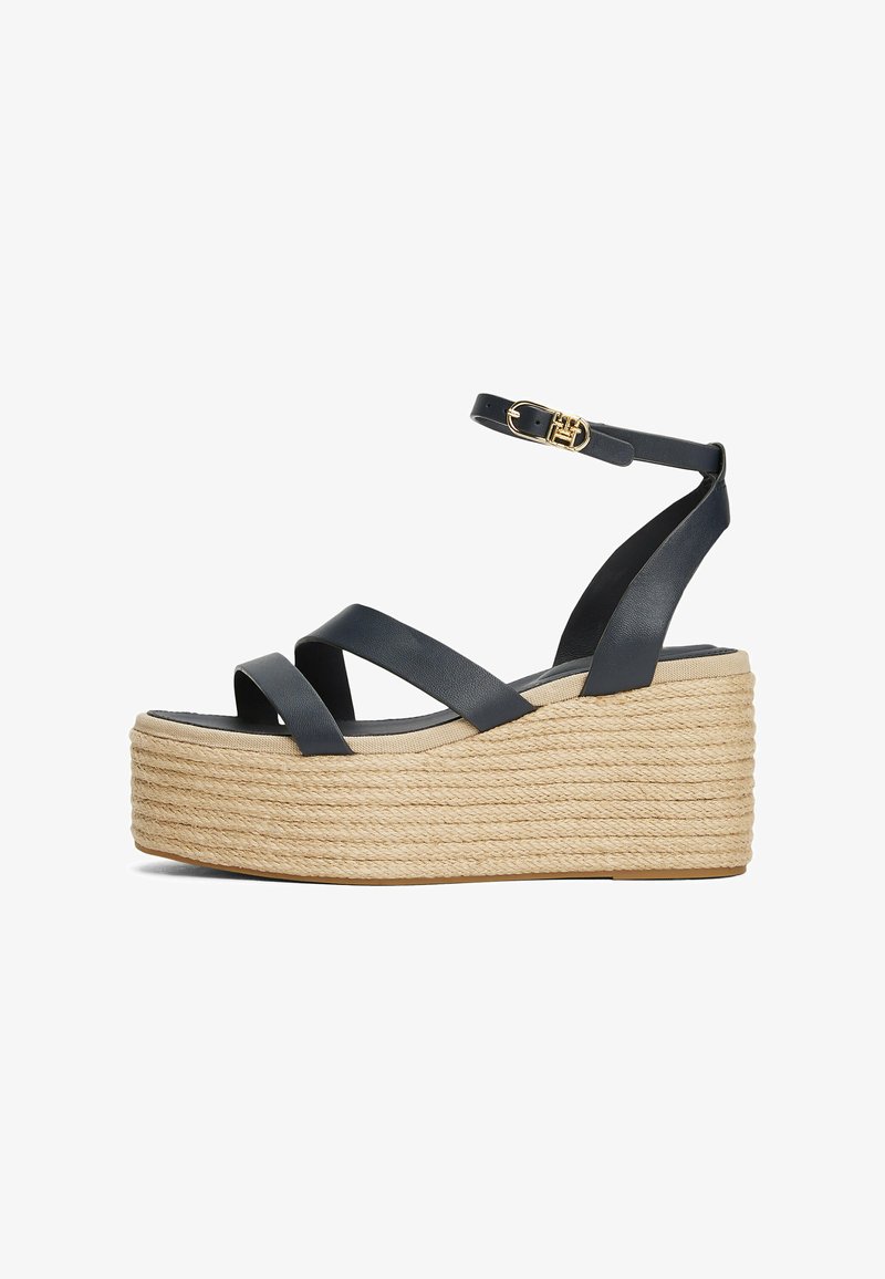 Sandali con zeppa in pelle nera, con cinturini incrociati e una piattaforma in corda intrecciata. Presentano una cinghia alla caviglia e dettagli con fibbia color oro.