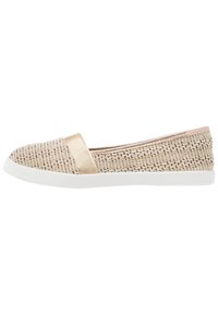 Platt slitsko med en texturerad beige övre del, guldaccentband och vit gummisula. Har en minimalistisk design och låg profil.