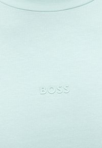 Ανοιχτό μπλε ύφασμα με ανάγλυφα, τονικά γράμματα "BOSS" τοποθετημένα στο κέντρο κοντά στην πάνω περιοχή του στήθους ενός ενδύματος.