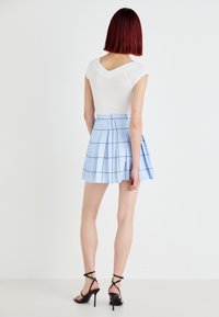 Top bianco aderente con maniche corte abbinato a una mini gonna plissettata azzurro chiaro con motivo a quadri e dettagli neri. Scarpe con tacco nere a strappi.