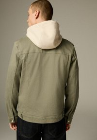 Khaki roheline jakk beežist kapuutsist. Kangas on sile, tagaküljel on nööbi sulgemine ja see omab juhuslikku lõiget. Tagant vaadates on nähtavad õmbluse detailid.