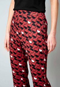 Rode broek met een patroon van een cirkelontwerp in zwart en wit, gemaakt van een gladde, lichte stof met een getailleerde pasvorm.