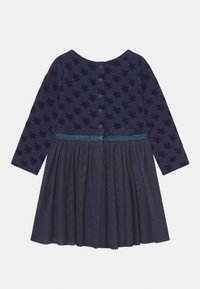 Vestido de marinheiro com mangas longas, padrão em forma de estrela, saia em camada de tule, faixa decorada com glitter azul e fecho de botão nas costas.