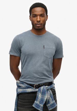 Lichtblauw katoen T-shirt met een ronde hals, korte mouwen en een borstzak. Draagt een blauw en wit geruit shirt, geknoopt om de taille.