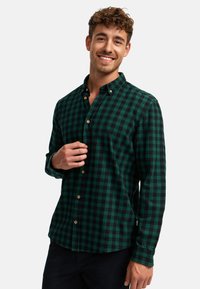 Zelená a černá kostkovaná košile na knoflíky vyrobená z flanelové látky, s klasickým límečkem a zakulaceným lemem, ozdobená dřevěnými knoflíky.