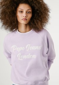 Fialová mikina s kruhovým výstrihom vyrobená z jemnej tkaniny, s bielym vyšitým textom "Pepe Jeans London" a raglánovými rukávmi.
