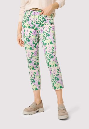 Femme portant un pantalon à motifs floraux verts, lavande et crème, longueur cheville, avec des mocassins beige et un pull beige clair.