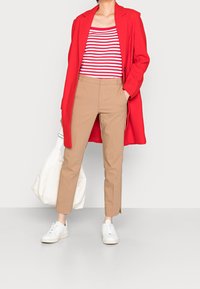 Rød lang frakke, hvid og rød stribet bluse, beige slim-fit bukser, hvide sneakers og beige taske. Glat tekstur, moderne snit.