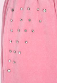 Roze fleece stof met een gladde textuur, versierd met rhinestones van verschillende groottes die in een patroon op het oppervlak zijn geplaatst.
