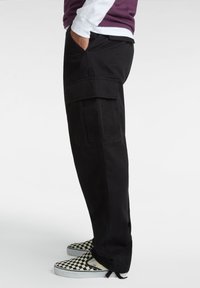 Schwarze Cargo-Hosen mit Seitentaschen, aus strapazierfähigem Material; figurbetontes Design mit leicht lockerer Passform; kombiniert mit karopartien Slippern.
