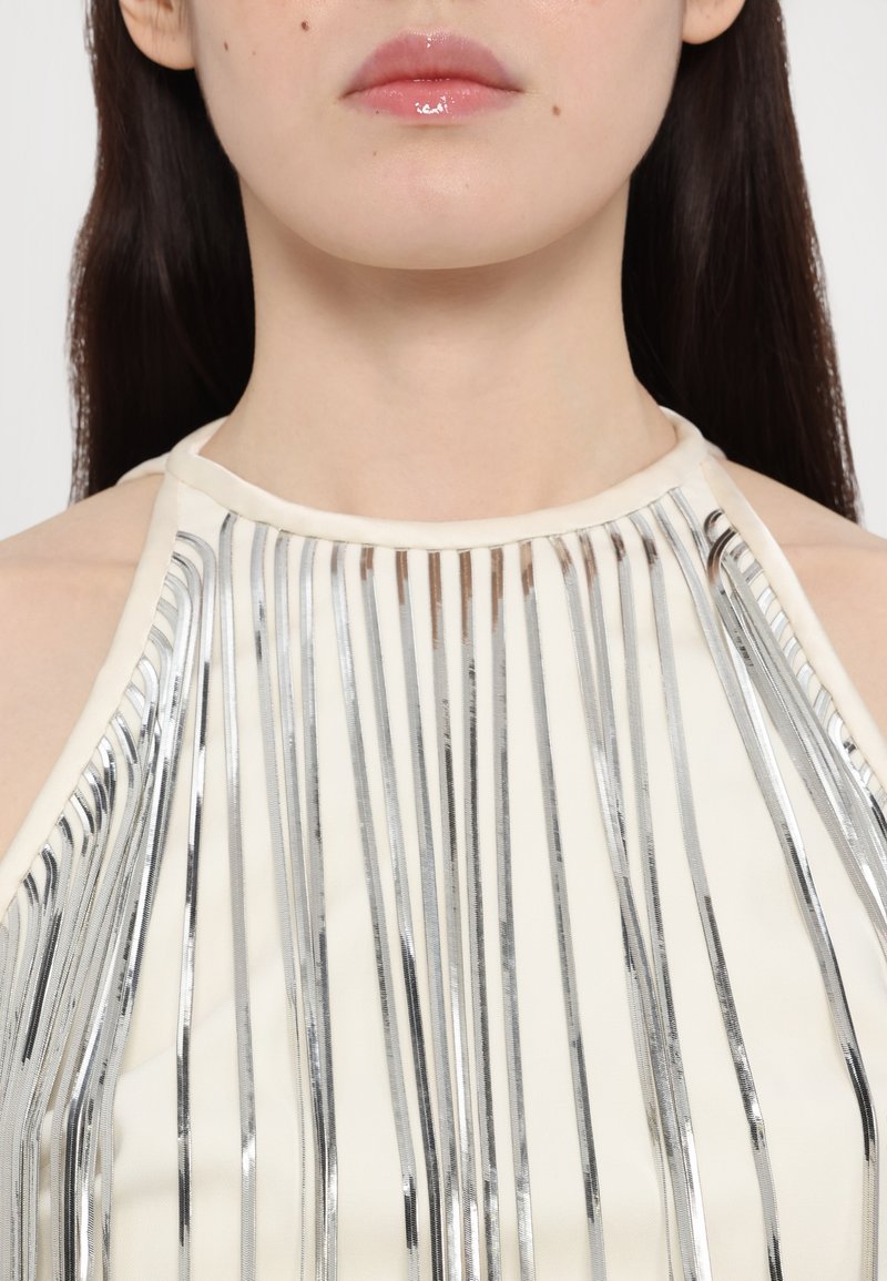 Halterneck-Top aus hellcremigem Stoff mit vertikalen silbernen Metallstreifen, die eine glatte Textur und ein elegantes Design betonen.