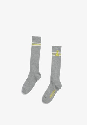 Graue knielange Socken mit geripptem Muster, die oben zwei weiße und einen gelben Streifen sowie ein gelbes Logo an der Seite aufweisen.