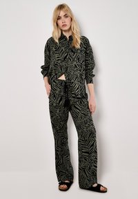 Black and green leaf-patterned outfit featuring a loose, collared shirt and wide-leg pants, made from soft fabric. Accented with drawstring.