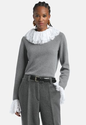 Siv sweater z belo čipkastim ovratnikom s volančki, z dolgimi rokavi in čipkastimi detajli na manšetah. V kombinaciji s sivo teksturirano hlačami in črnim pasom.