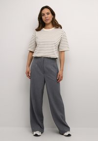 Gestreepte shirt met korte mouwen in crème en taupe, gecombineerd met grijze wijde broek en witte sneakers. De outfit heeft een relaxte stijl.