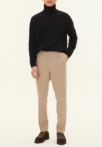 Maglione a collo alto navy, pantaloni beige con pieghe e scarpe marroni stringate con suole testurizzate. Design semplice e palette di colori neutri.